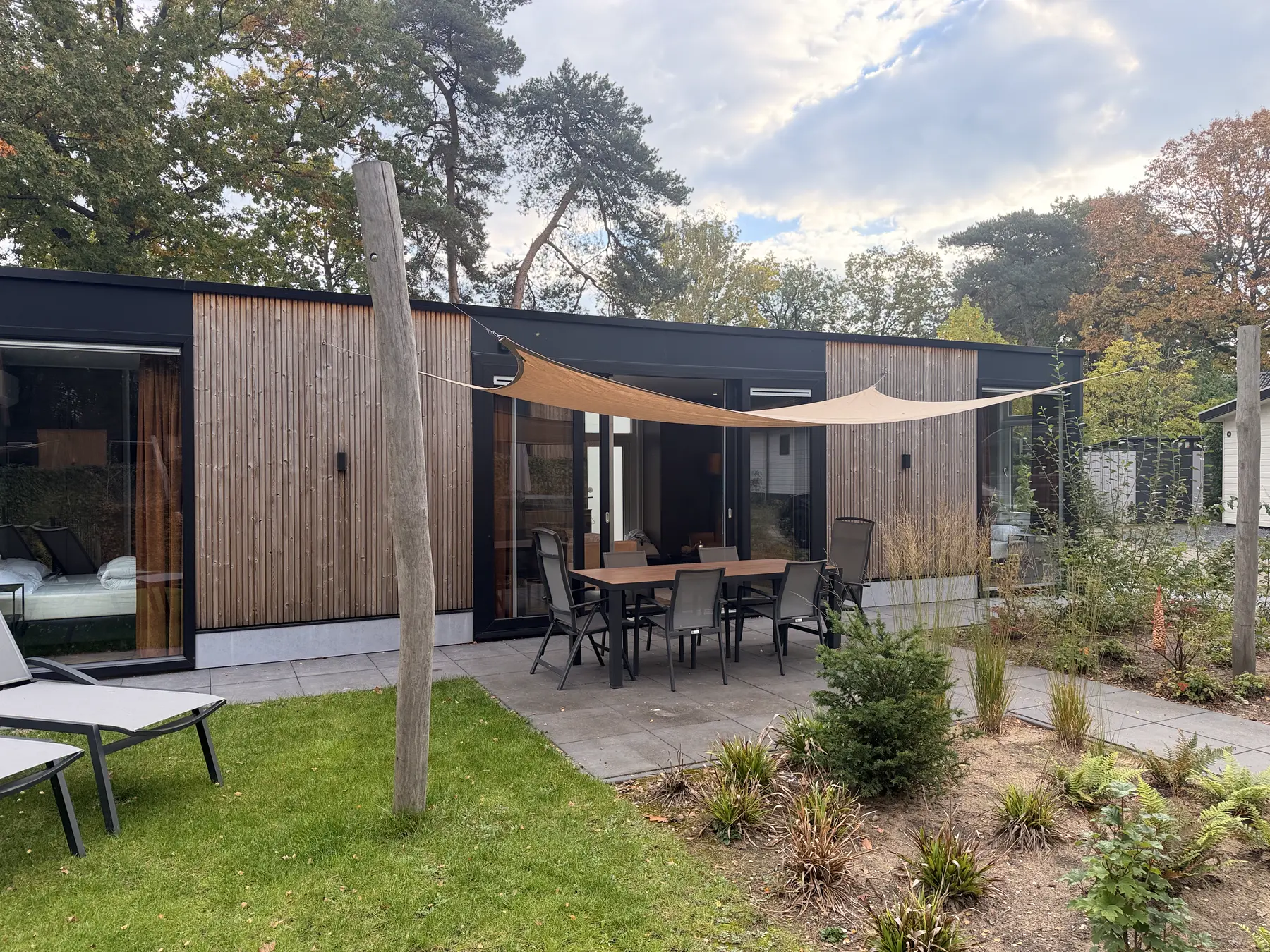 De lodge vanuit de tuin, met terras, schaduwzeil en ligbedden op het gras